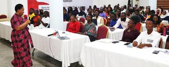A speaker addressing a seated audience of young women and men at a gender and youth inclusion session